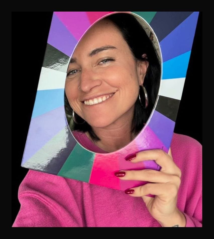 Erica Renzoni sorride tenendo davanti al viso una cornice con i colori dell'arcobaleno.